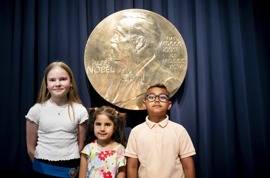 Three children standing in front of a big Nobel Prize Medal