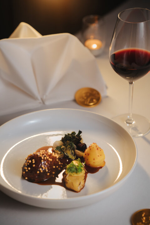 En tallrik med mat samt vikt linneservett, Nobelmedalj i choklad och ett glas vin
